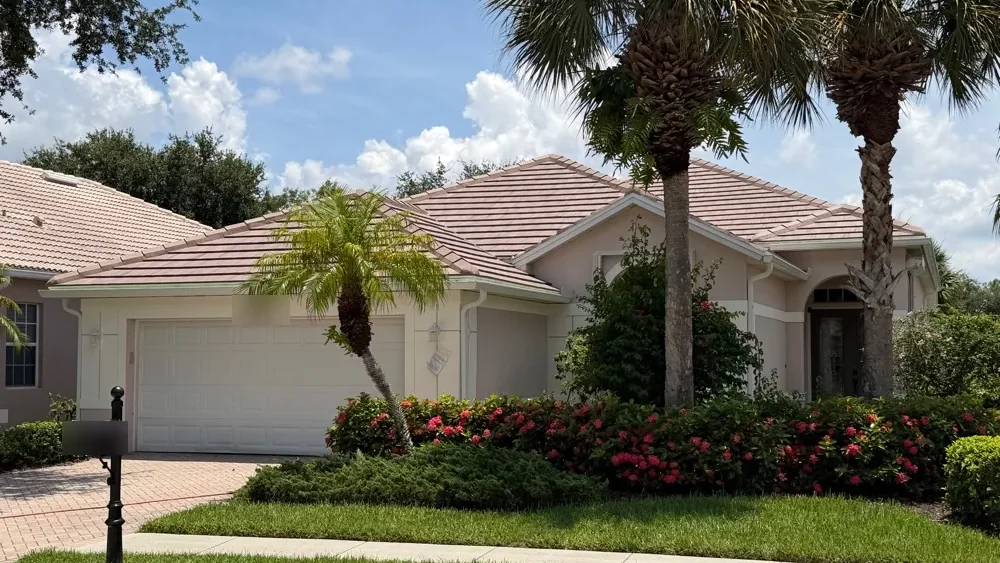 Single-story Naples home with tile roof and new white seamless gutters, framed by palms