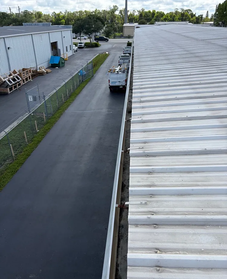 Rooftop view of a cleaned gutter running the length of a metal warehouse roof in Fort Myers, FL