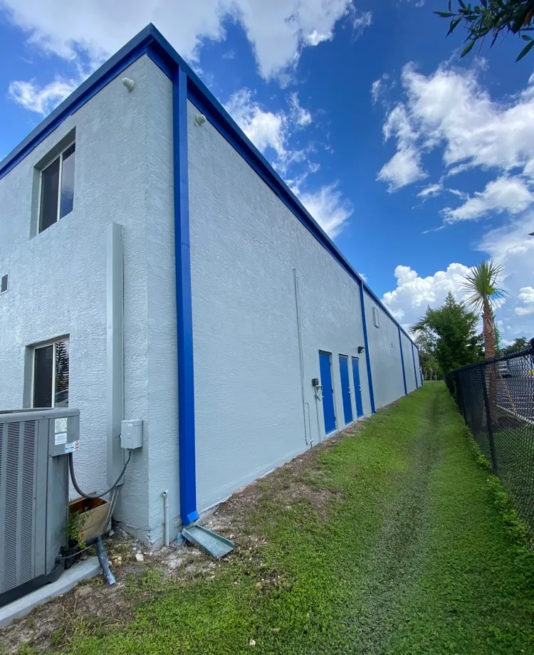 Commercial building wall with downspouts ending at the foundation before rerouting in Cape Coral, FL