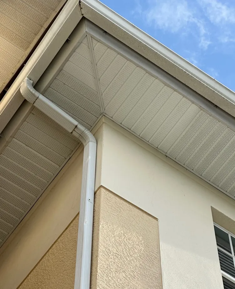Close-up of new white vented aluminum soffit at a roof corner with downspout in Cape Coral, FL
