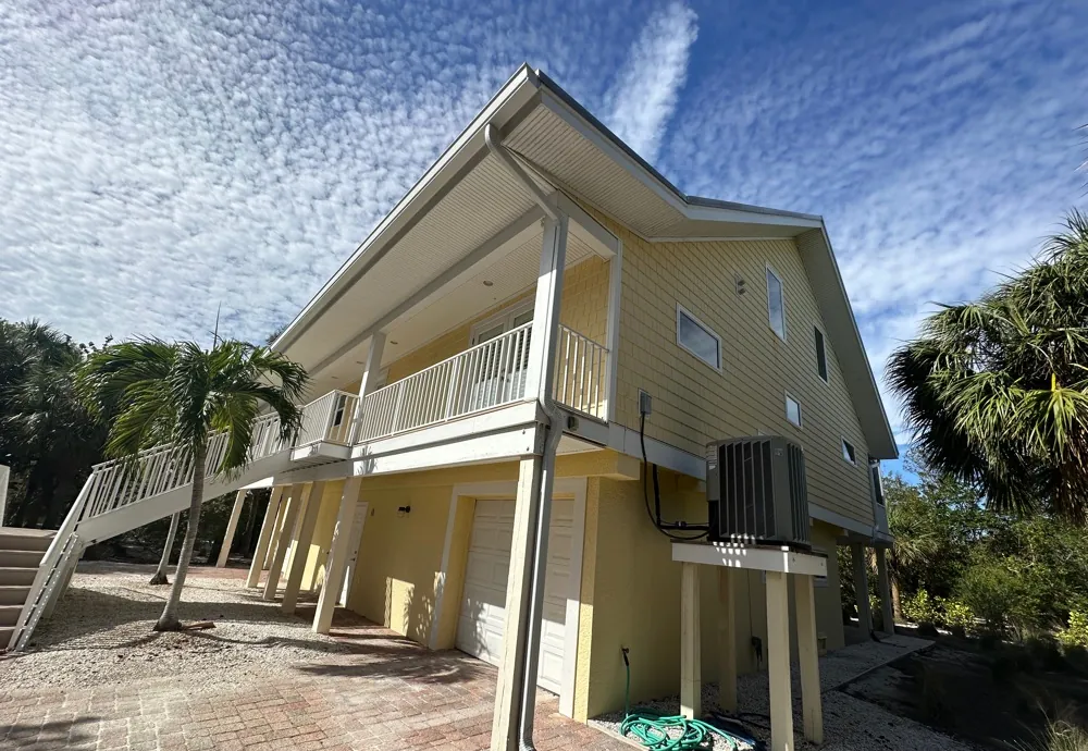 Side of a raised yellow home with a white downspout in Sanibel, FL